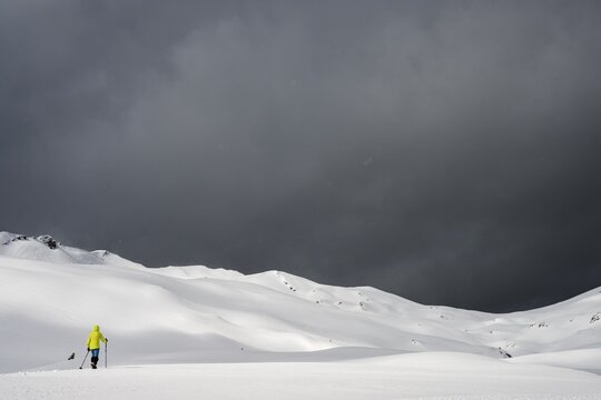 Ski tourer on a vast plateau with snow-covered mountains in the background and dramatic sky, Berlinger K&ouml;pfle, Ritzlern Kleinwalsertal, Vorarlberg, Austria
