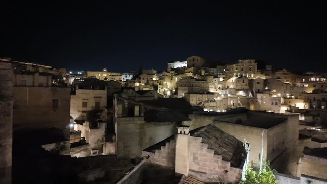 Breathtaking panoramic view of the ancient city of Matera (Sassi di Matera) at night, beautifully illuminated with warm golden lights. UNESCO World Heritage Site in Basilicata, Southern Italy. 4k