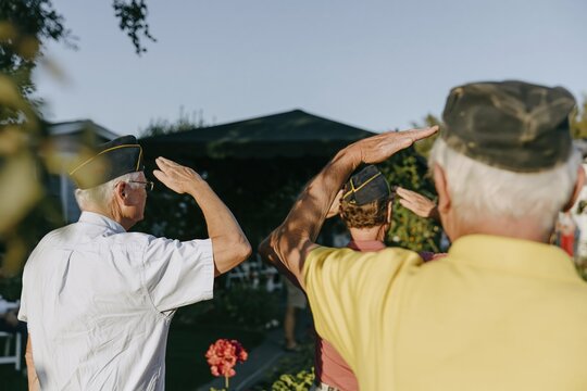 Veterans in dark service caps salute during a dignified outdoor memorial ceremony, featuring worn fabric textures for remembrance and honor