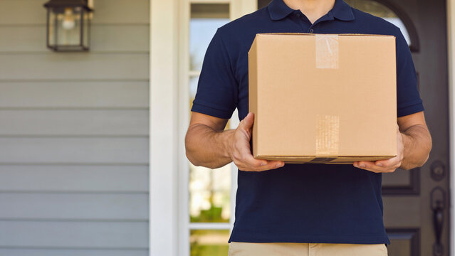 Delivery man holding a cardboard box in front of a residential house front door for shipping service