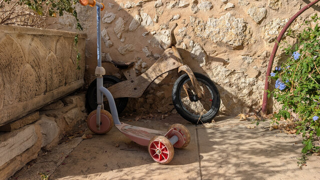 Children's scooter and wooden balance bike beside a stone wall. 