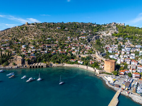 High angle view of Alanya historic peninsula, red tower, shipyard, moored boats and coastal landscape in Antalya, Turkey. Mediterranean blue sea, architecture and sunny blue sky.