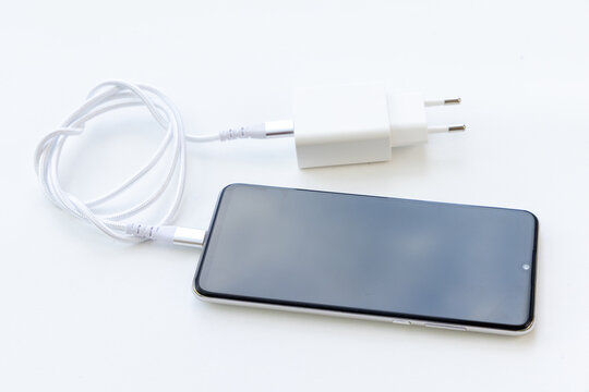 Modern smartphone connected to wall charger with white cable