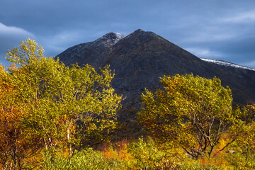 Scenic autumn landscape of Khibiny mountains with rocky peaks under dramatic stormy sky and golden birch trees, Kola Peninsula, Russian Arctic. © sablinstanislav
