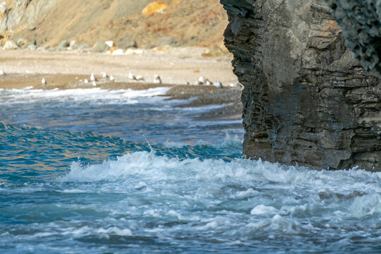 Ocean waves, rock cliff, sandy beach create a tranquil coastal scene with crashing waves