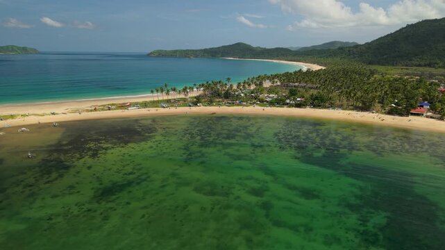 Drone footage over Nacpan and Calitang Twin Beach in El Nido, Palawan, capturing the distinctive shape of the two beaches, white sand shoreline and surrounding tropical landscape.