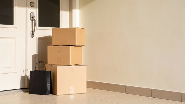 Stack of cardboard boxes and black shopping bag delivered at the front door of a residential home under bright daylight