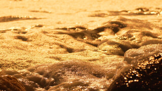 Golden waves sparkle over dark rocks at sunset close up beautiful warm light on the ocean shore