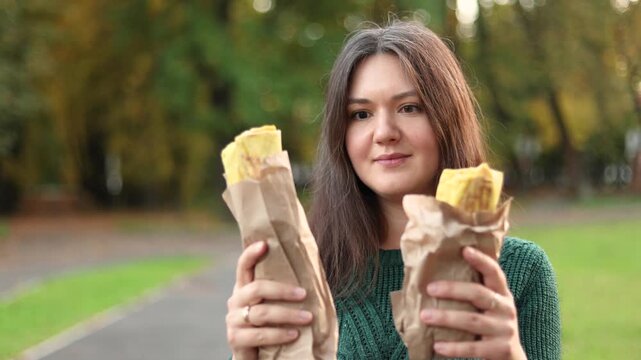 Close up shows young woman holding large and small shawarma wraps. She hesitates while deciding which Turkish kebab she wants to eat.
