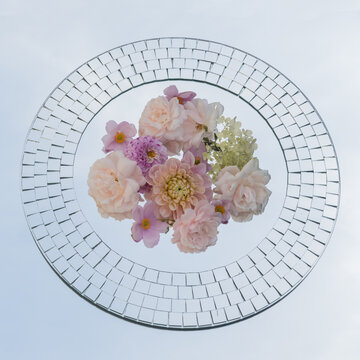 abstract arrangement of white and pink flowers on round mirror reflecting the sky