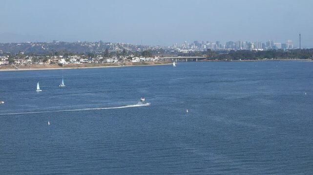 A wide view of Sail Bay in San Diego California featuring sailboats speedboats a bridge and the distant downtown city skyline under a clear blue sky