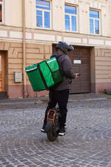Food delivery courier riding an electric unicycle with insulated delivery backpack through a city street. Mobile courier uses a smartphone while transporting orders for last mile delivery and urban fo © A-Quantix