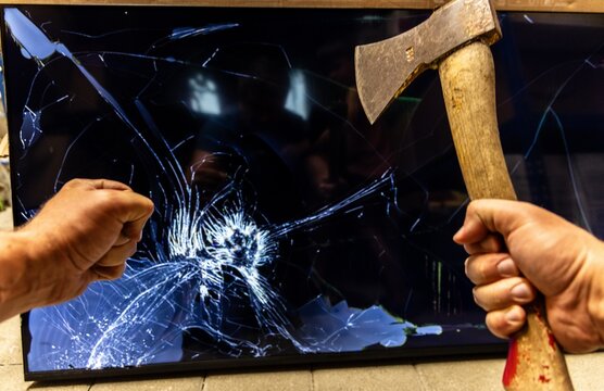 Angry person destroying a television screen with an axe