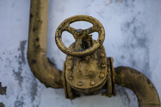 Old rusty valve and pipe on a faded wall, showcasing industrial