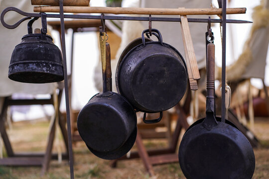 Hanging cast iron cookware at an outdoor reenactment camp. Cast iron pans and traditional cookware in a reconstructed historical camp setting.