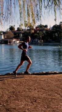 Athletic man jogs around a small lake in Los Angeles. Vertical video.