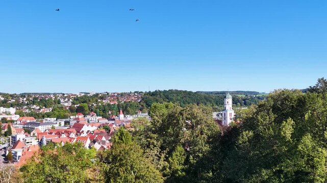 Malerische Panorama-Luftaufnahme von Biberach an der Ri&szlig; mit der historischen Altstadt, markanten Kircht&uuml;rmen und herbstlichen B&auml;umen unter blauem Himmel.