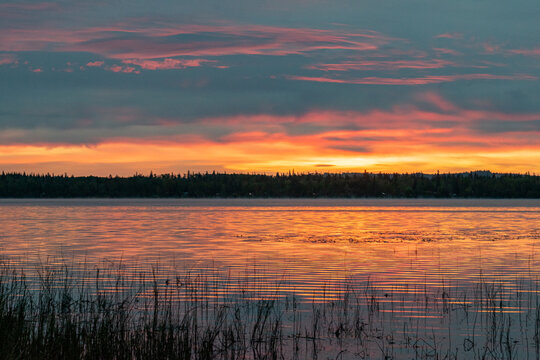 Cloudy orange sunset over calm lake with reflections in water