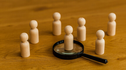 Wooden figures arranged on a table with one figure magnified by a magnifying glass