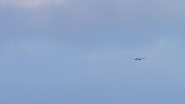 Passenger jet on final approach with landing gear down and landing lights on, head on view against overcast cloudy sky, telephoto shot