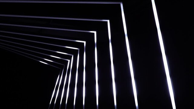 Illuminated neon light lines creating geometric tunnel perspective in a dark indoor architectural setting with structure