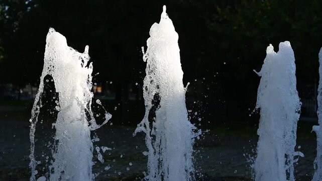 Close-up video of powerful fountain jets shooting upward, with white water streams and droplets captured against a dark background. The dynamic movement, splashing water, and changing shapes create an