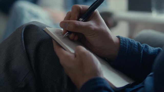 Hands of unrecognizable male therapist using pen to write notes in notebook during professional psychology consultation. Close up view