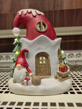 Christmas gnome standing near lighted ceramic house figurine with led lights