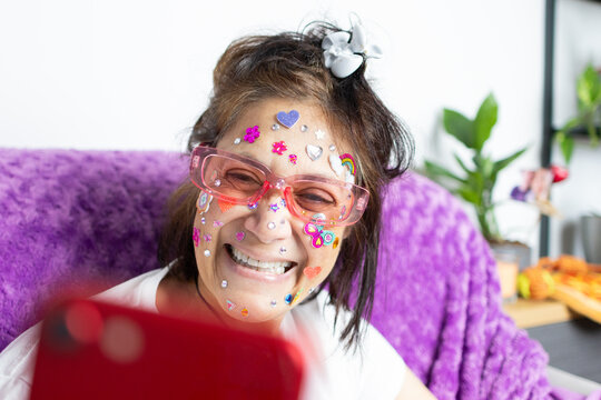 Middle eastern woman wearing face colorful stickers, smiling and taking a selfie with a red smartphone