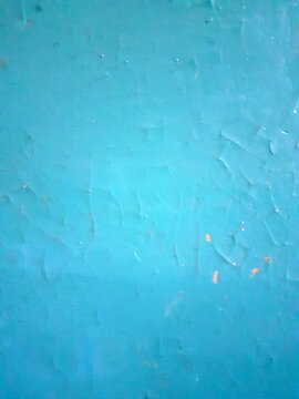 Weathered Cyan Cracked Paint Surface Background. Vertical photo of a wall painted blue, featuring chips and cracks.