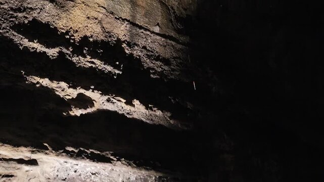 Close-up of water drops falling down from the ceiling of a dark volcanic lava cave.
