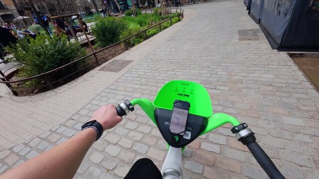 POV riding a rental electric bike along a wide pedestrian boulevard with plane trees and city buildings in the Eixample district on an overcast day, Barcelona, Catalonia, Spain