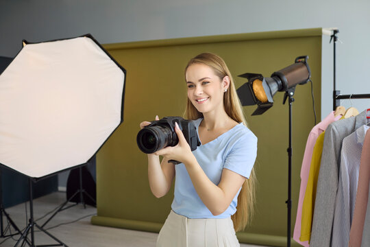 Photographer woman with camera in studio photoshoot. Modern lighting and equipment frame a fashion portrait set with backdrop, softbox and strobe. Concept is creative professional studio work.