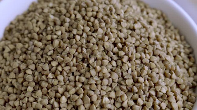 Raw buckwheat grains inside white bowl moving closer to camera macro shot, 4K