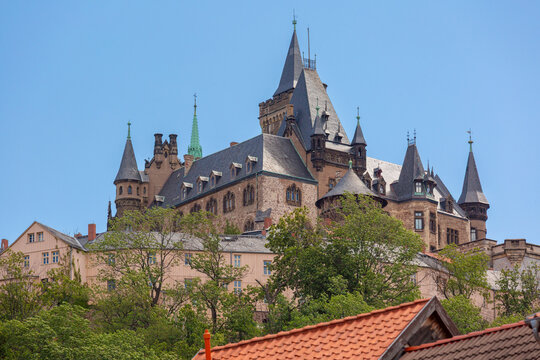Impressive historic architecture with towers and ornate details rising above the rooftops and trees of Wernigerode, Germany.