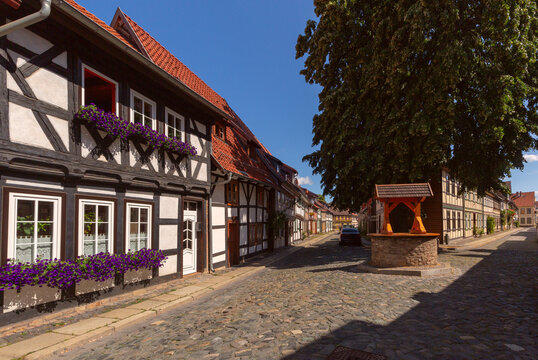 Picturesque cobblestone street with traditional half-timbered houses, colorful flowers and an old stone well in Wernigerode, Germany.