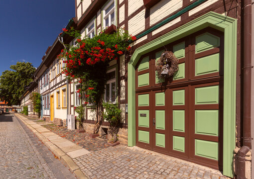 Colorful traditional half-timbered houses with decorative facades, red tiled roofs and flowers along a cobblestone street in Wernigerode, Germany.