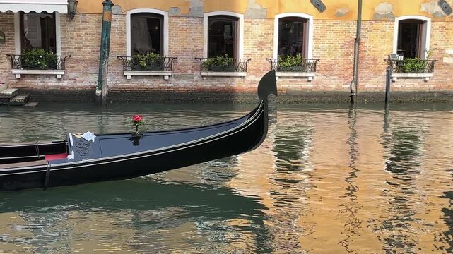Close up view of  traditional black gondola prow with metallic fero gliding across a calm water canal reflecting historic Venetian facades in Venice, Italy.