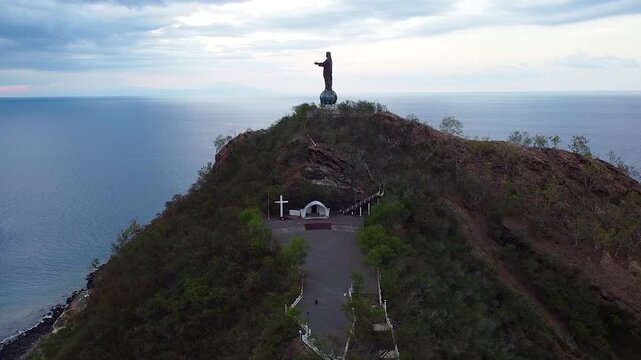 Aerial rising Cristo Rei statue of Jesus Christ with crucifix cross with ocean views in capital city Dili, Timor-Leste, Southeast Asia