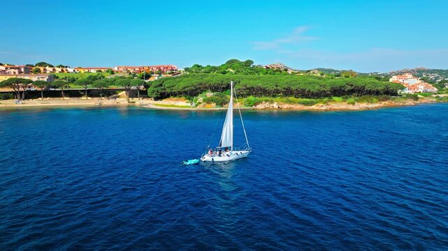 Drone view of Palau in Sardinia, Italy. Sailing boat, deep blue Mediterranean water, coastal town and green shoreline create a peaceful seaside travel scene.