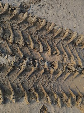 Top view close up of heavy machinery tire tracks pattern imprinted on wet muddy ground at a construction site.