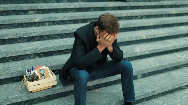 Redundant adult male sitting on concrete stairs covering face in deep agony. Financial insecurity panic