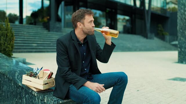 Fired adult male drinking beer on corporate stairs near box. Alcohol abuse coping mechanism