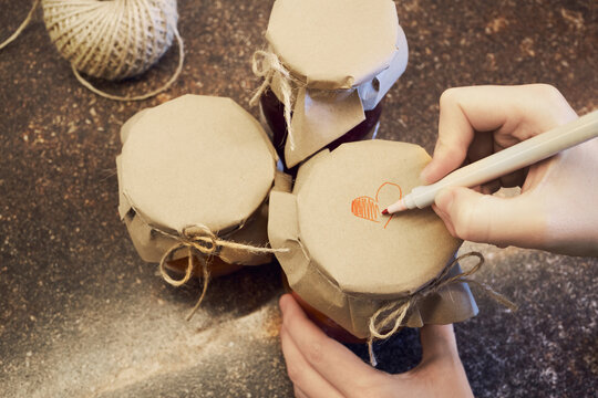 Hand decorating jars of homemade preserves with heart drawing for thoughtful gift