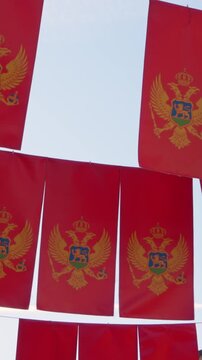 Strings of red flags with the golden double headed eagle emblem hang in rows above a sunny street and sway gently in the breeze, festive decor for a town event season.