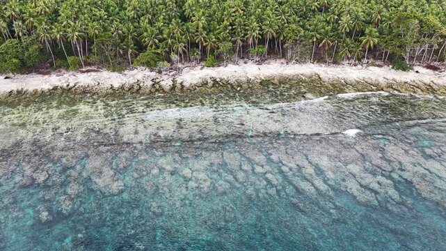 Calm seas bathe the beautiful coastline of the remote Maju Island in the Molucca Sea, Indonesia. A rugged, rocky reef surrounds this tropical paradise which few people ever visit.