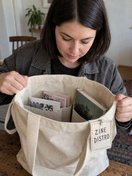 Woman Opening Canvas Tote Bag Filled with Zines for Distribution