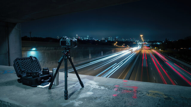 Camera on a tripod capturing long exposure light trails on a highway at night with digital camera mounted sitting concrete ledge traffic busy highway night lens case
