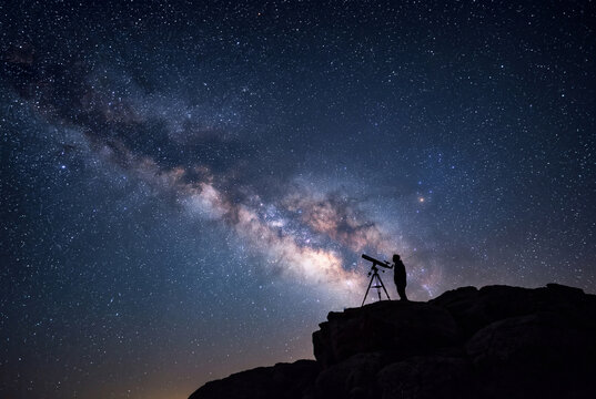 Stargazer observing the Milky Way at night on a rocky hill