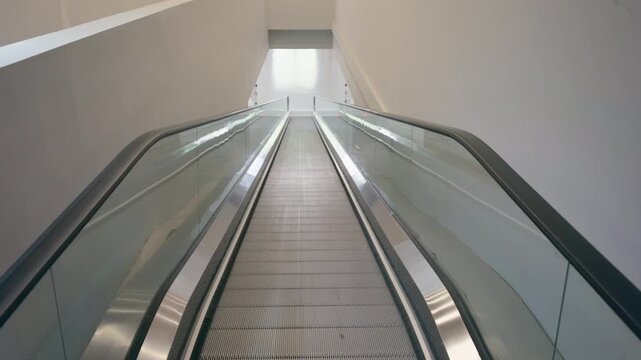 A symmetrical, high-angle view of a long escalator leading towards a bright, minimalist white space. The composition highlights clean lines, metallic textures, and geometric symmetry in a modern